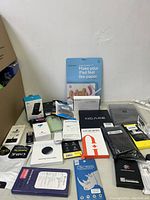 Wide view of the lot showing cell phone cases, screen protectors, chargers, and converter boxes on a white surface