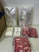Clear plastic gift bags of varying sizes stacked and packaged, shown with red twist ties in multiple packs.