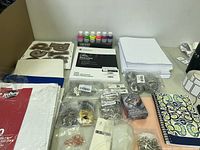 Overview of craft supplies including paint set, paper pads, jewelry findings, cloth pieces, and notebooks