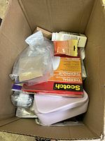 Top view of the box showing laminated pouches, acrylic medium, plastic containers, and other crafting materials.