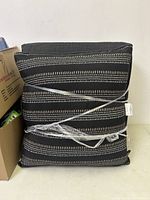 Set of stacked cushions wrapped in plastic showing black fabric with white dotted stripes.