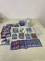 Wide shot of all trading cards spread out on table including unopened packs, sports cards, game cards, and card protectors.