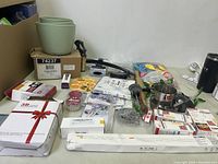 Overview of all miscellaneous household items including bowls, cookware, kitchen tools, LED bulbs, and small boxed items laid out on table.