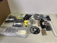 Full lot arranged on table showing various small hardware, tools, and consumables including sanding discs, black plastic hardware packs, yellow tape dispenser, drill bit set, and metal discs.
