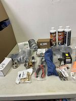 Lot of miscellaneous automotive tools, parts, and fluids showing bottles, metal fittings, pliers and other small components.