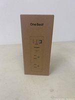 Front of brown cardboard box featuring One Beat branding and a simple product line drawing.