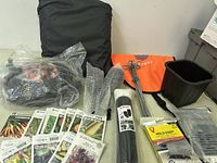Multiple gardening items including seed packets, garden stakes, plant ties, and containers all arranged on a white surface.