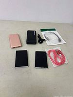 Photo showing four power banks in different colors along with a coiled black charging cable, a packaged white adapter cable, and a packaged pink-red USB charging cable.
