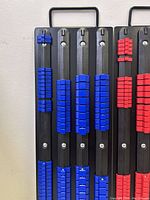 First photo shows one black socket holder with blue clips for smaller sockets and a handle for carrying, set against a wall.