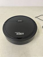 Top view of Sweepin Robot mini vacuum showing the round black body with a central start button and Sweepin Robot branding.