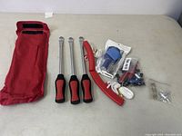 Full view of tire tool set including three slide hammer style tire irons, two red plastic tire levers, assorted valve tools and accessories, and red fabric carrying pouch.