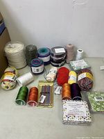 Front view of yarn skeins, thread spools, crochet hooks, and fat quarter fabric packs arranged on a white surface.