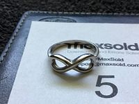 Photo of a 14k gold infinity ring resting on a MaxSold branded card, showing the front of the ring and its infinity symbol shape.