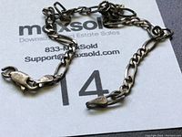 Full length of the sterling silver chain with lobster clasp laid on paper.