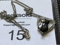 Photo showing the pendant on the necklace with two cats inside a heart shape, silver and black textured design.