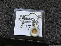 Photo showing the entire silver chain and circular light green jade pendant with gold-tone symbol in middle