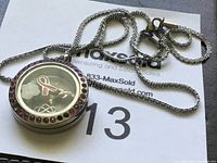 Clear photo of round sterling silver locket with red gemstones around the edge and keepsake charms inside.