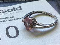 Side view of sterling silver ring with pink round gemstone placed on a MaxSold paper background.