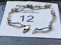 Photo showing full length of a sterling silver bracelet with pink rectangular gemstones set along the chain, and lobster claw clasp.