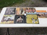 Front view of 6 vinyl album covers on white table outdoors