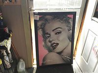 Photo showing full view of the large framed Marilyn Monroe art print leaning against a wall, near a door and cleaning supplies.