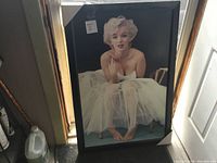 Full view of large framed Marilyn Monroe print resting against a wall on the floor, showing the image, frame, and corner protectors.