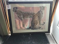 Framed artwork with two leopards, standing and sitting, clear details and visible reflection of surroundings in glass.