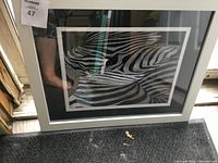 Framed abstract black and white zebra art with a focus on stripes in an artistic pattern, placed on a dark carpet near a door.