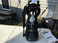 Front view of Be electric pressure washer with hose and spray wand attached, soap dispenser bottle mounted on front, showing overall unit design and control lever.