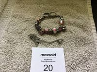 Full view of the charm bracelet with charms, two rings and a chain on a beige textured surface.