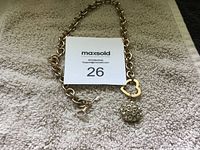 Image of gold-tone chain necklace with Guess logo charm and crystal cluster pendant laid on a textured beige surface along with a MaxSold lot card.