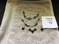 Full view of matching sterling silver necklace, bracelet, and earrings laid out on beige towel.