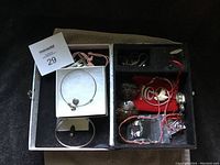 Interior photo of the jewelry box showing numerous compartments with various pieces of untested jewelry including bracelets and pendants