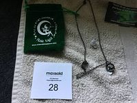 Full view of the necklace with pendant and pouch placed on a towel surface, showing the chain and spherical charm along with the velvet pouch and a small clear stone.