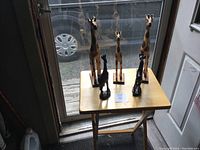 Five wooden giraffe statues arranged on a small wooden table near a glass door, showing variations in height and color.