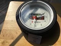 Wall clock with Wurth racing design shaped like a tire placed on a wooden table under natural light.