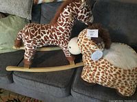 Wooden rocking horse and plush giraffe ride-on toy together on couch, showing overall condition and size