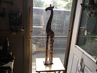 Wooden giraffe sculpture standing on a small table, showing full height and shape.