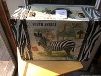 Front view of the wooden suitcase showing the zebra, giraffe, leopard, and travel graphics with zebra-patterned edges.