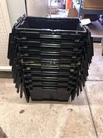 Stack of nine black rectangular plastic containers with built-in lids, viewed from stacked side.
