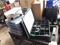 Stack of multiple clear plastic storage cases filled with assorted hardware including screws, nuts, bolts and washers.