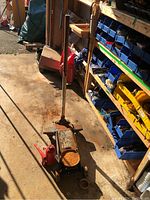 Photo showing vintage blue floor jack and red bottle jack side by side on garage floor with shelving in the background.