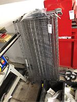 The metal wire shelves stacked vertically leaning against a red cabinet along with plastic parts and casters on the floor nearby.