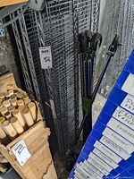 Metal NSF shelving unit unassembled, stacked wire shelves visible with four caster wheels leaning against the unit.