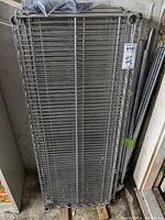 Stack of wire mesh shelves wrapped with plastic on a wooden pallet on the floor.