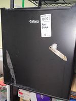 Front view of black Galanz mini fridge with label and visible scratches on door.