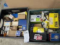 Black and green milk crates filled with assorted boxes of nails and screws, some boxes labeled and partially opened.