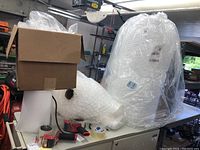 Packing supplies arranged on a table in a garage including bubble wrap rolls, box, tape rolls, and dispensers.