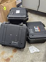 Four black Pelican Protector cases shown stacked and on the floor, three Pelican 1400 models and one Pelican 1450 model visible, with scuffs and wear marks.