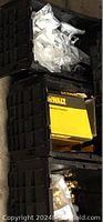 Top view of stacked black plastic bins containing sealed plastic bags with assorted plumbing parts and a Dewalt yellow box